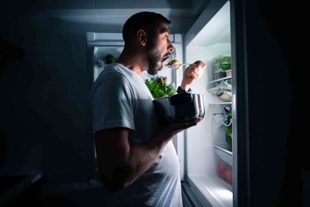 Uomo affetto da binge eating ha un attacco di fame notturno e mangia con foga davanti al frigorifero