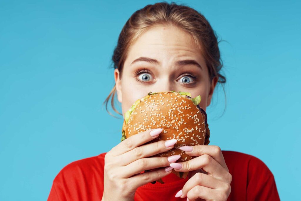 donna tiene in mano un hamburger, tipico cibo ultraprocessato