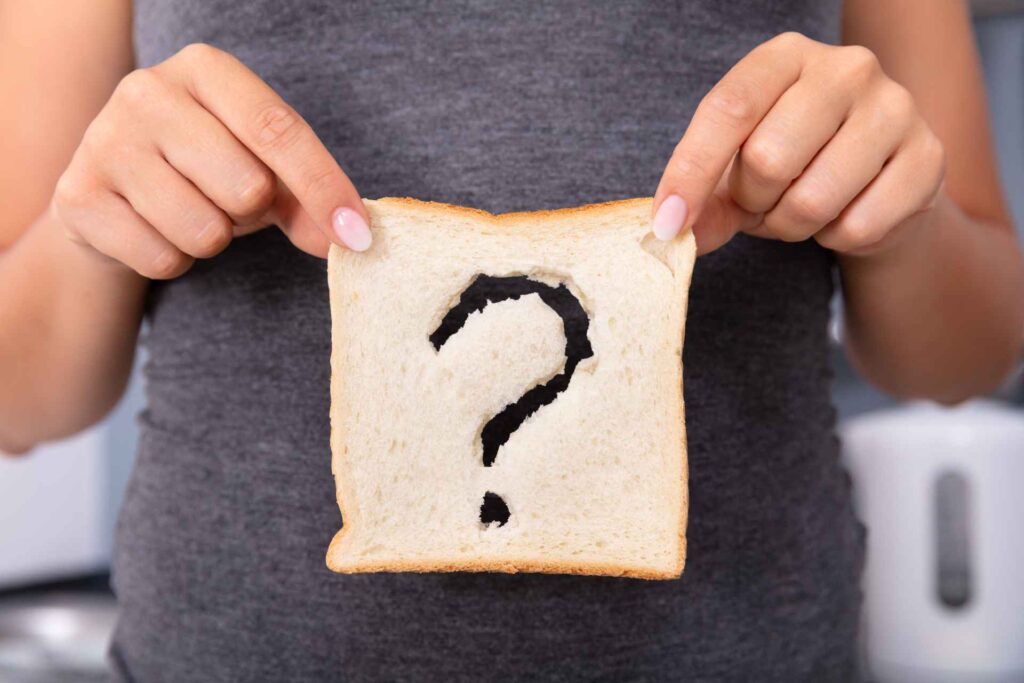 Donna con in mano una fetta di pane in cui è stato disegnato un punto interrogativo per indicare incertezza di sensibilità al glutine o celichia