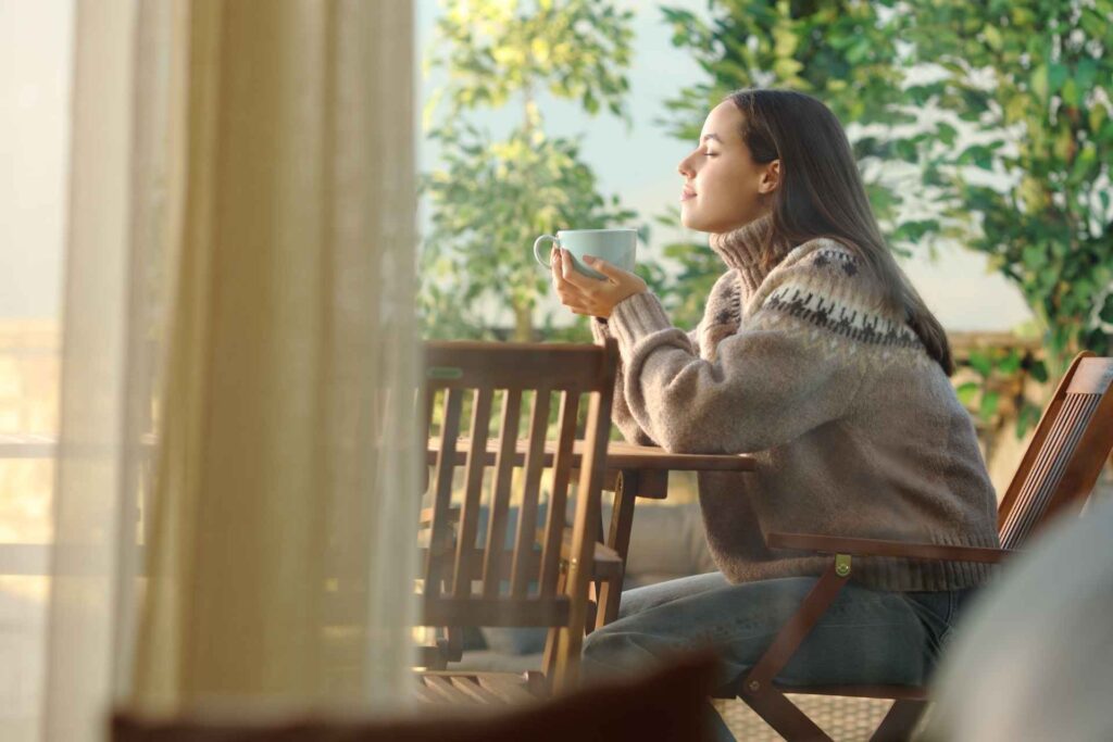 Donna fuori in balcone che prende il sole mentre beve un caffè in inverno per fare ricarica di vitamina d