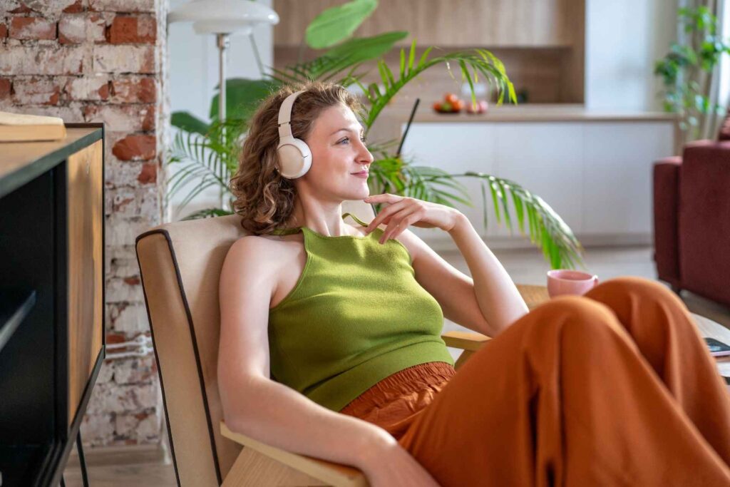Ragazza seduta su una poltrona ascolta in cuffia un podcast o della musica
